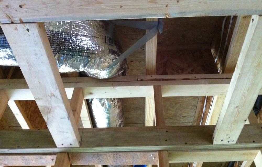 A flex duct running through these difficult-to-seal joists above a garage wall